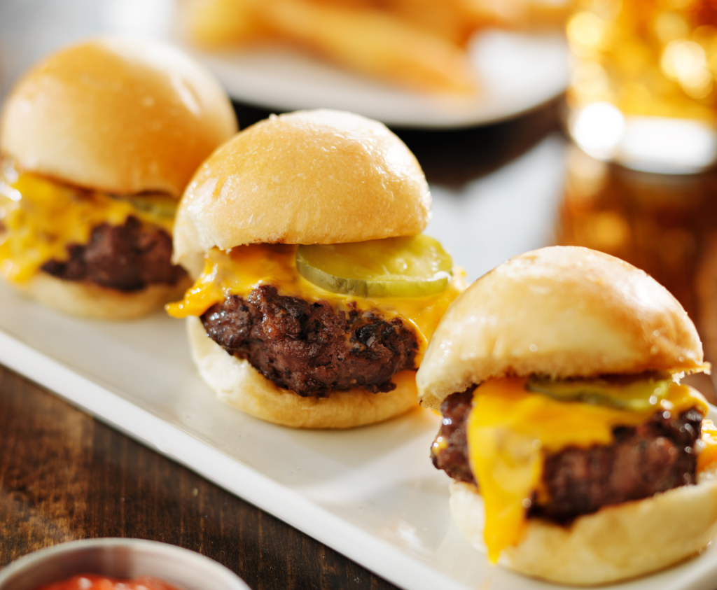 A stylish serving platter filled with mini Wagyu beef sliders, each nestled in a glossy brioche bun. The burgers are layered with melted cheese, pickle, and a dollop of tangy aioli, with the marbled beef patty peeking through. -Classic Catering - Mini Wagyu Burgers - finger Food Menus-Catering a Party at Home